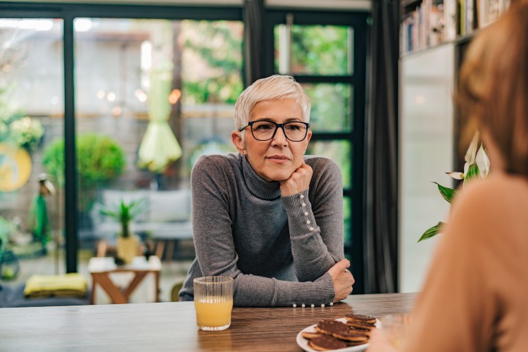 woman listening to woman across a table with a drink and biscuits on it